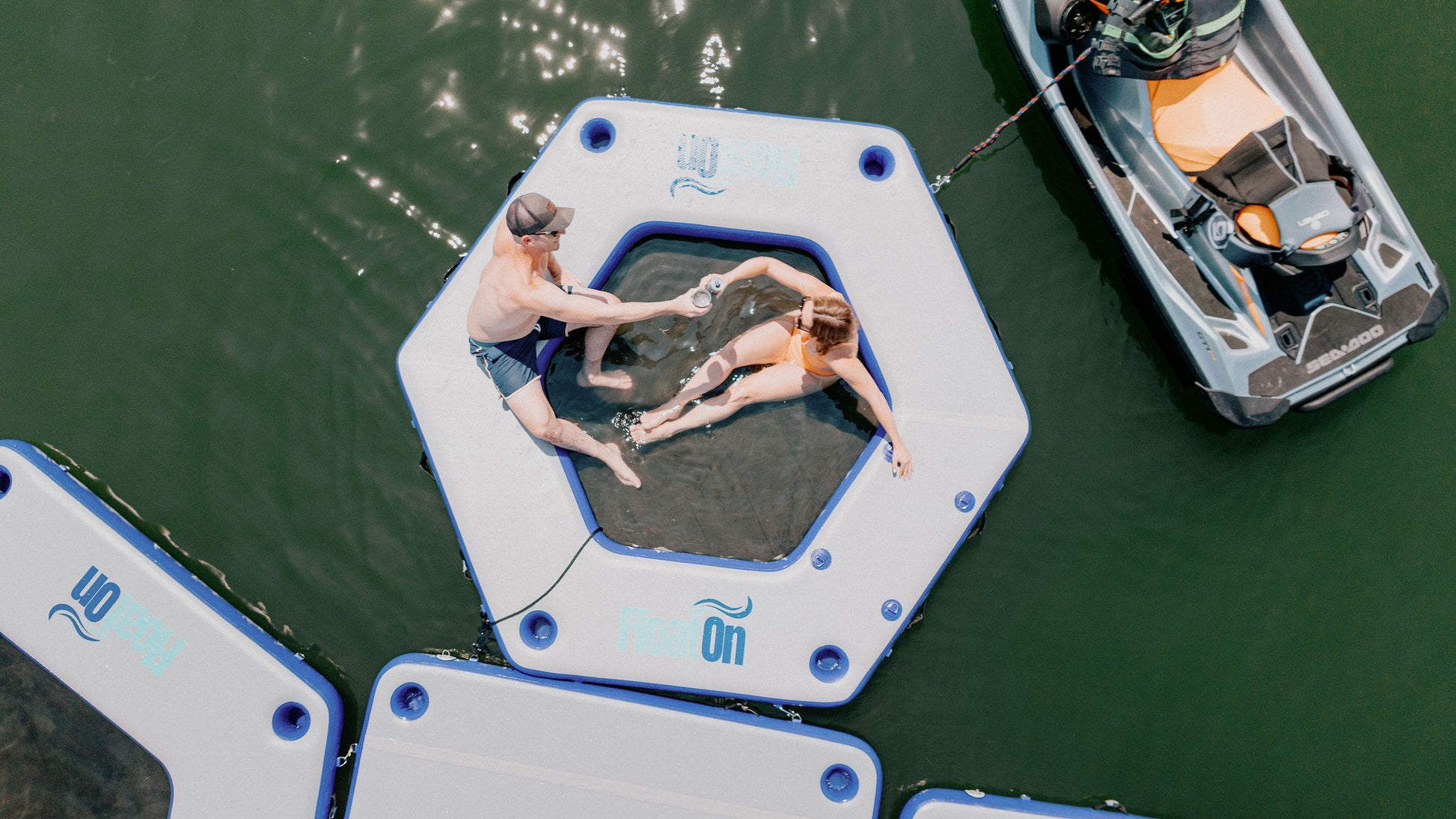 A man and a woman toasting their drinks on the Oasis water mat from Float on.