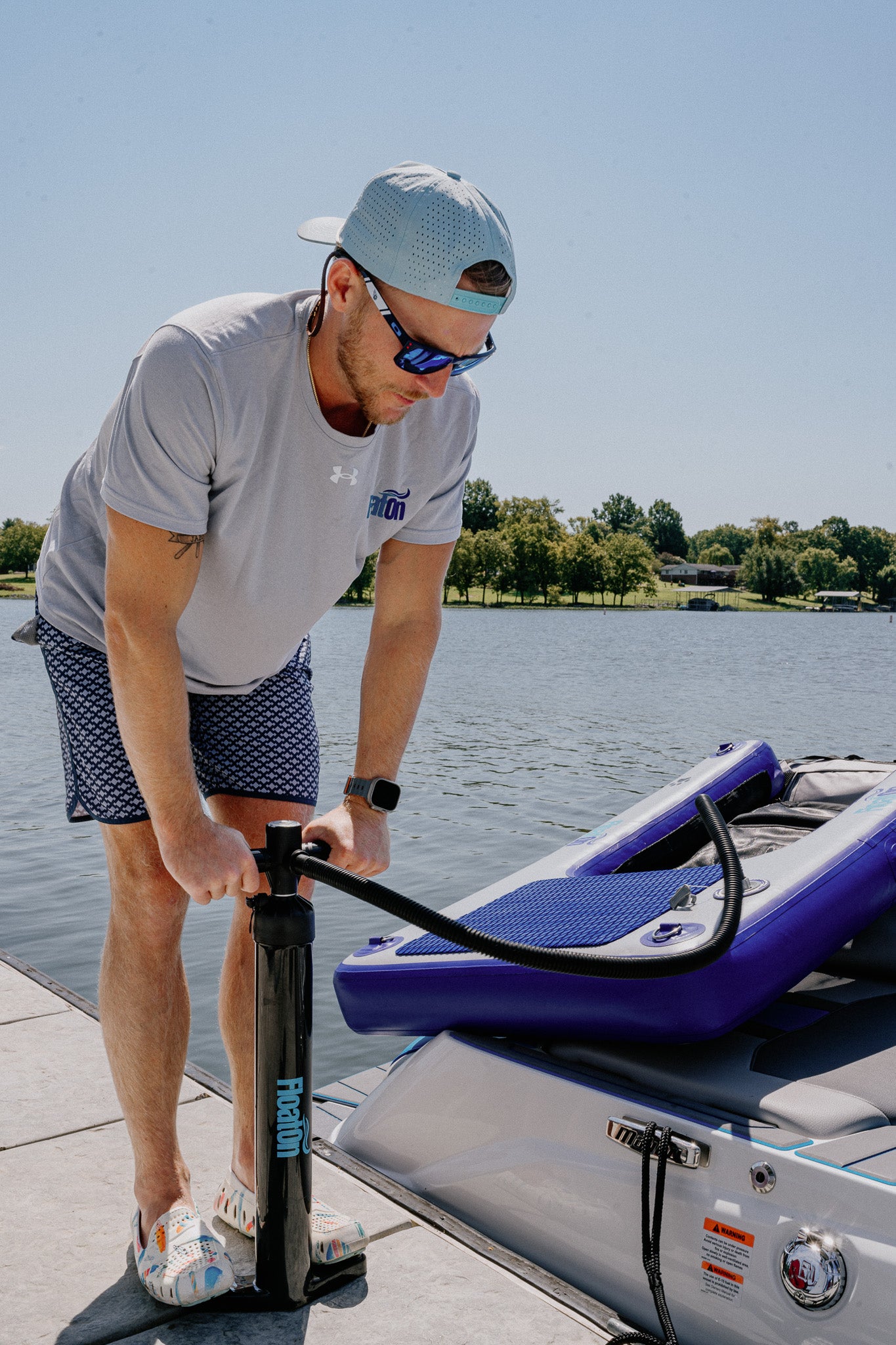 A man standing on a dock filling up their Grand Oasis inflatable water mat with air.