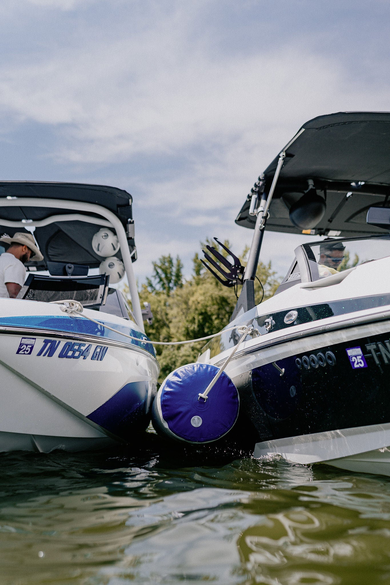 A man standing on a boat talking to another man on another boat with an attached inflatable boat fender.